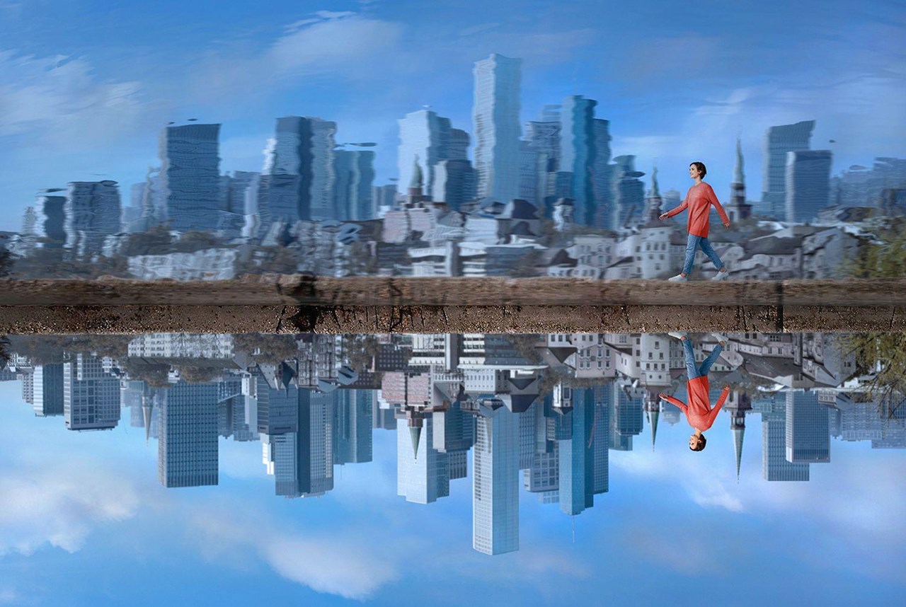 Mann in rotem Shirt geht auf einem schmalen Weg entlang einer Wasserfläche, die die Skyline einer Stadt reflektiert.