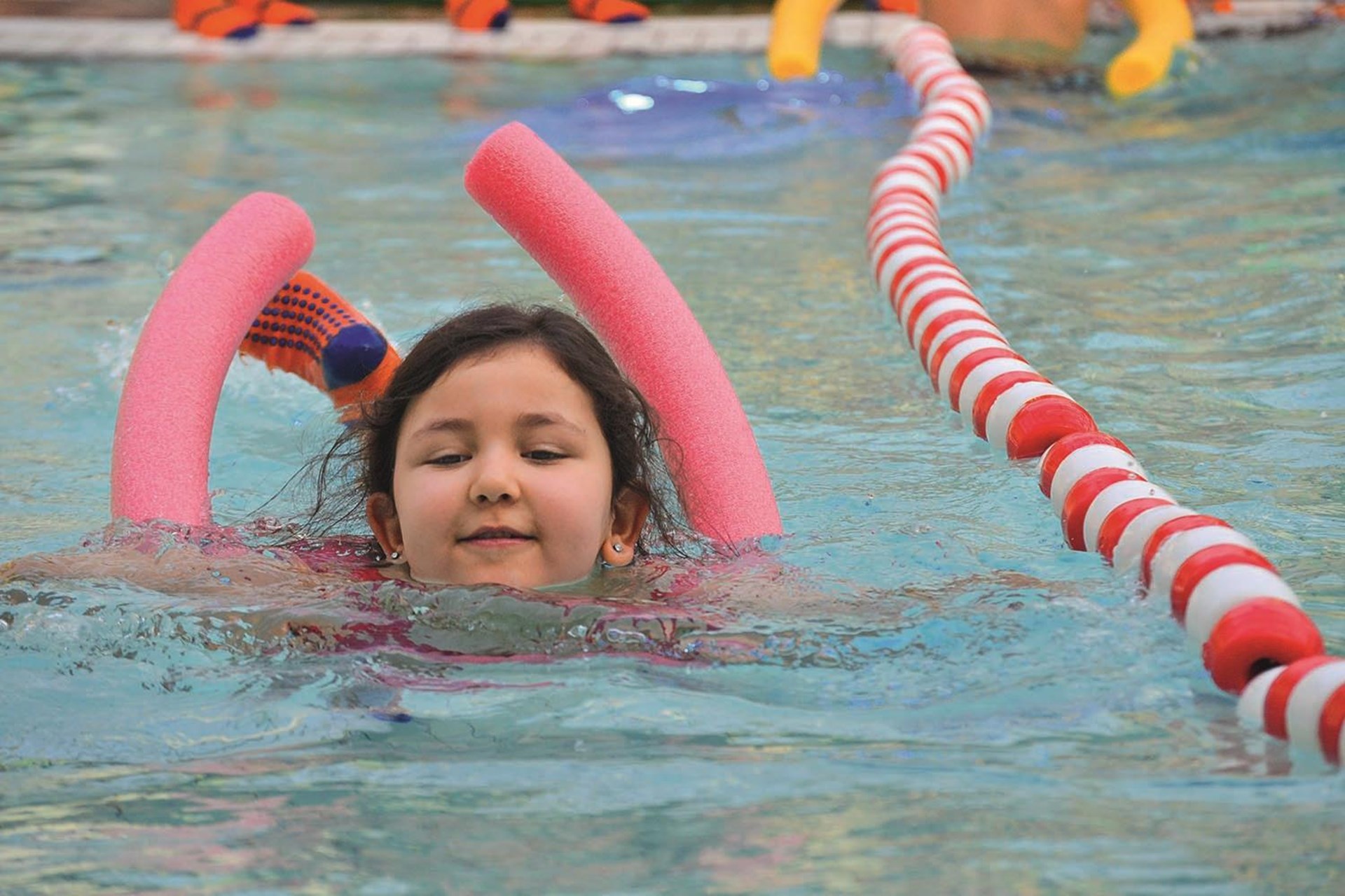 Ein Mädchen mit einer Schwimmhilfe aus Schaumstoff im Wasserbecken.