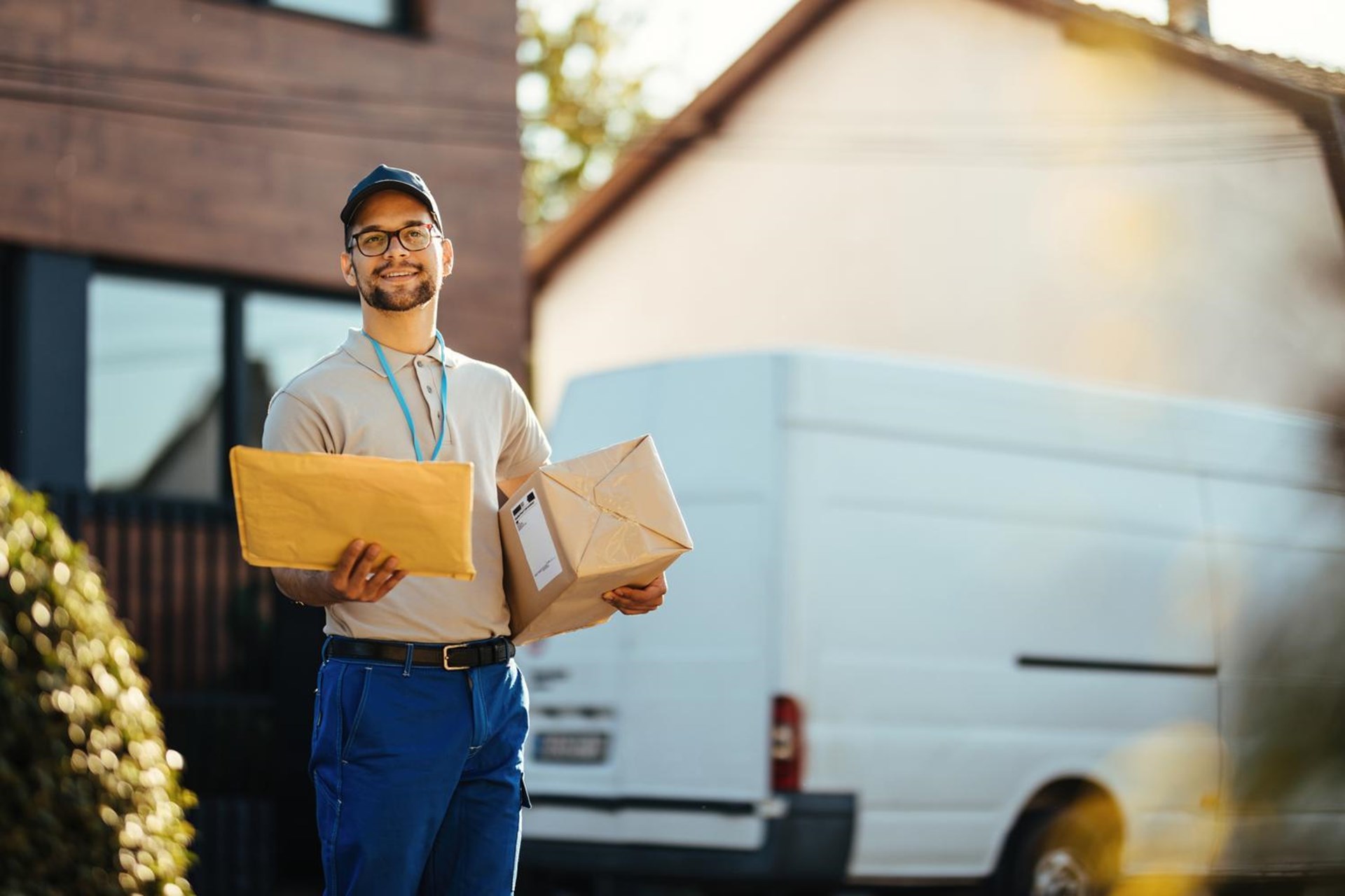 Ein uniformierter junger, freundlicher Mitarbeiter eines Paketdienstes mit Briefen in der Hand.