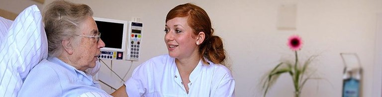 Eine Pflegerin bei einer alten Dame am Pflegebett