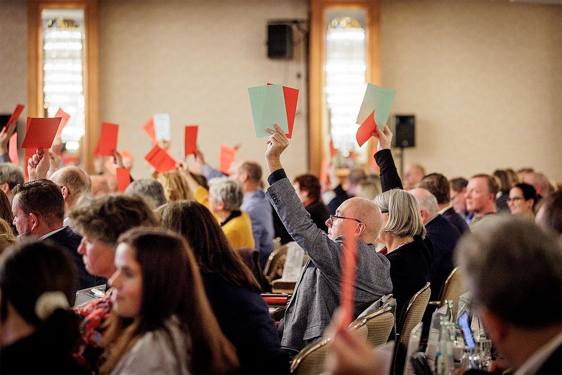 Teilnehmer einer Konferenz heben rote und grüne Karten zur Abstimmung in einem großen Saal.