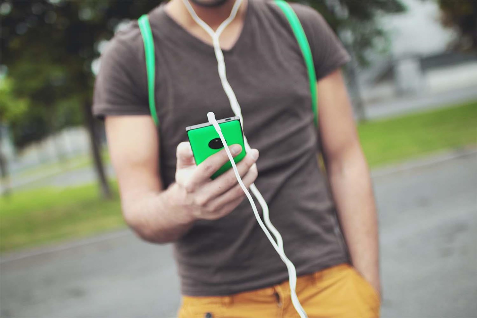 Junger Mann mit Handy in der Hand, in dem Kopfhörer stecken.