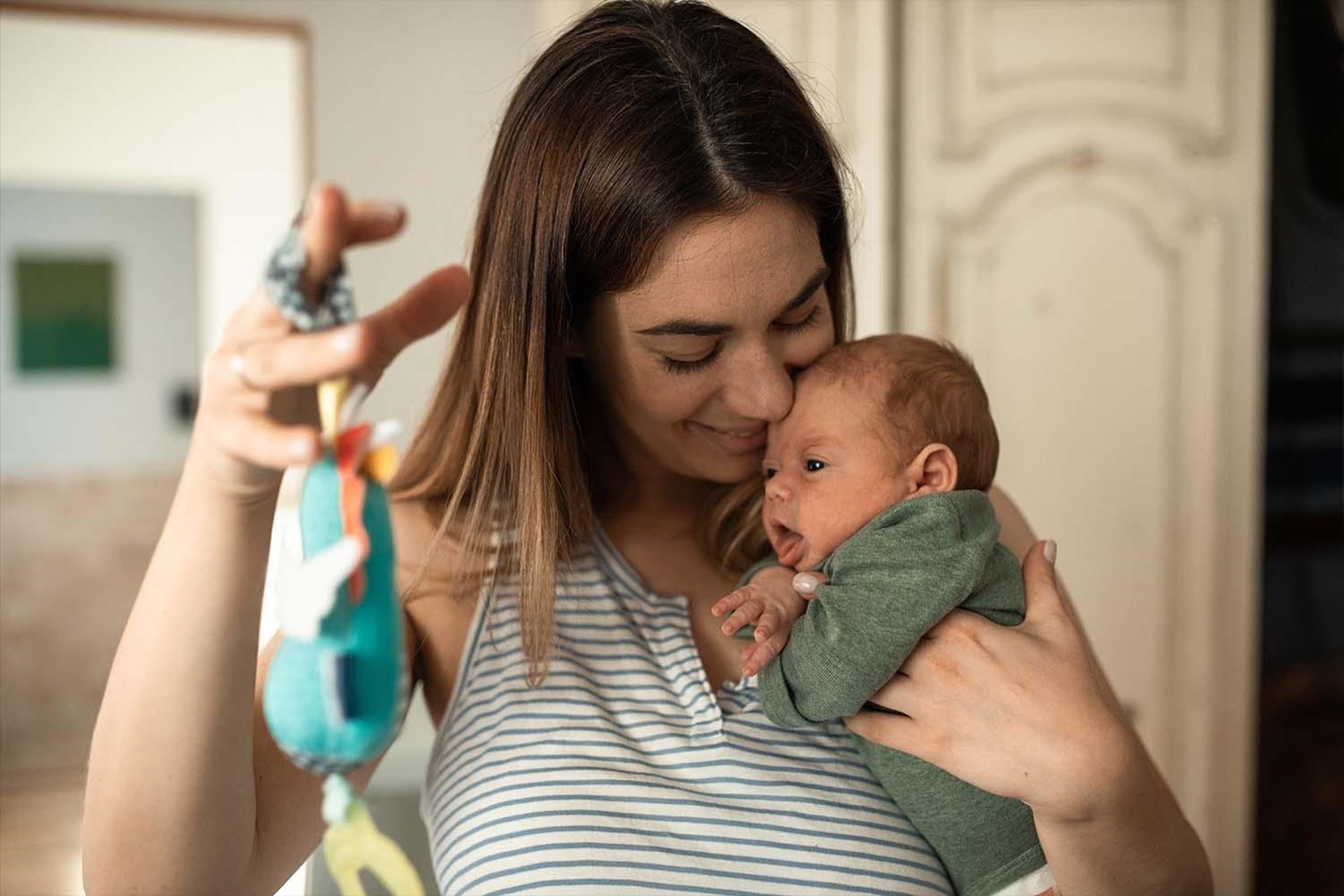 Eine junge Frau mit längeren braunen Haaren hält ein Baby auf dem Arm.