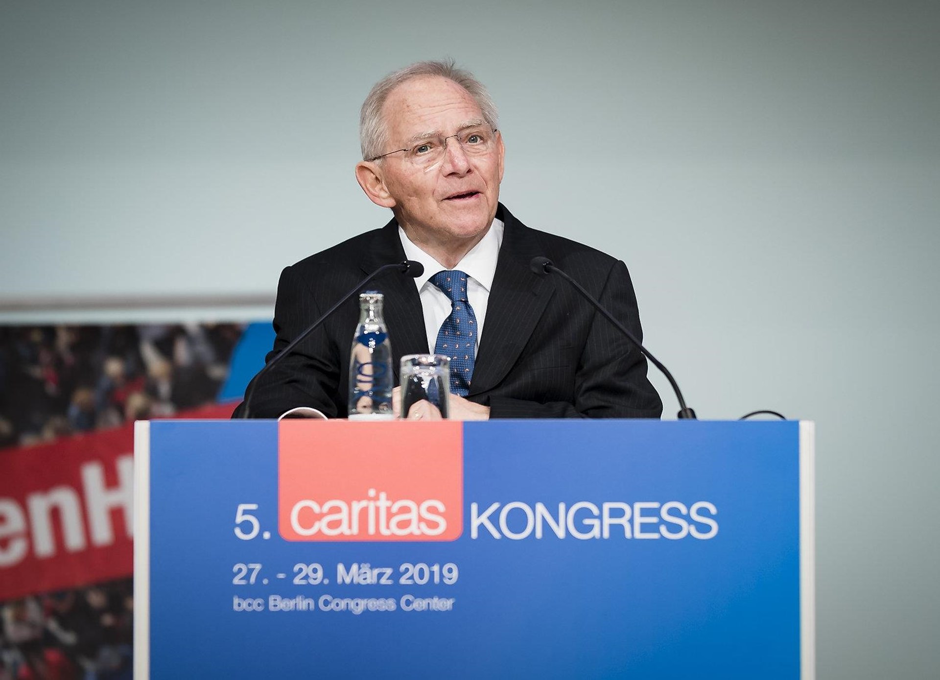 Wolfgang Schäuble in Anzug spricht am Rednerpult beim 5. Caritas Kongress in Berlin, 2019. Hintergrund zeigt das Kongresslogo.