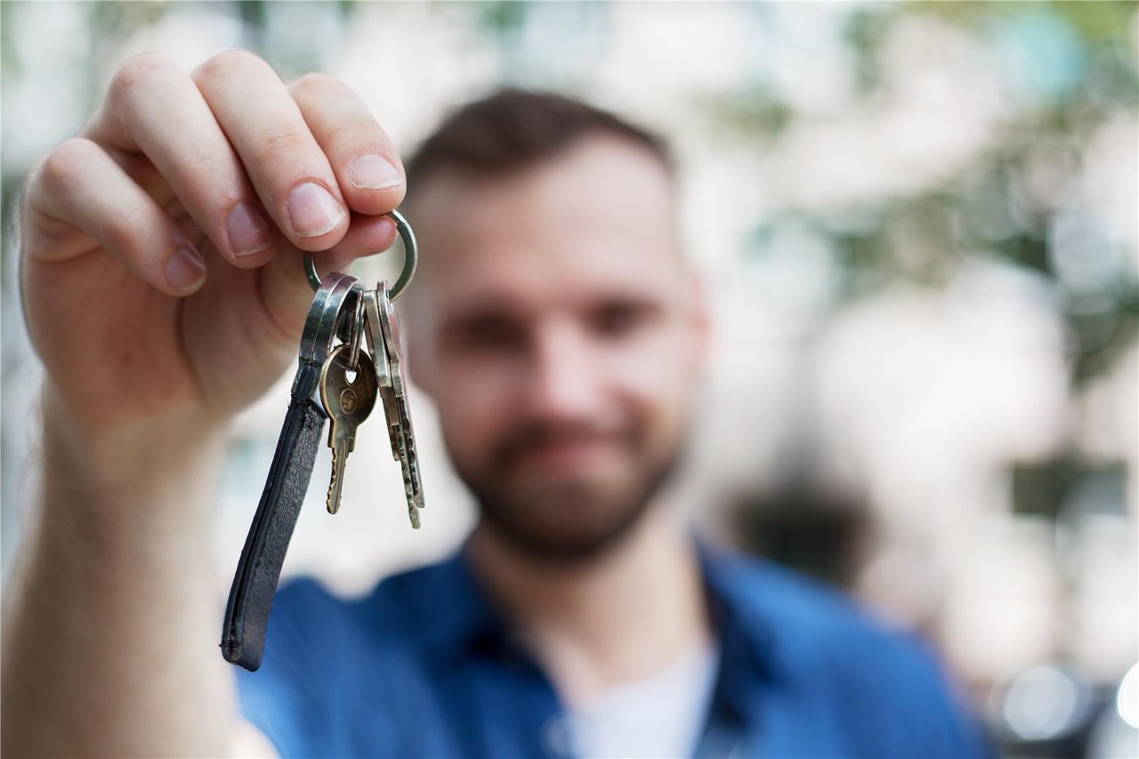 Mann hält einen Schlüsselbund mit mehreren Schlüsseln in der Hand, unscharfer Hintergrund.
