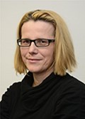 Lächelnde Frau mit hellblonden Haaren und Brille, die schwarze Kleidung trägt