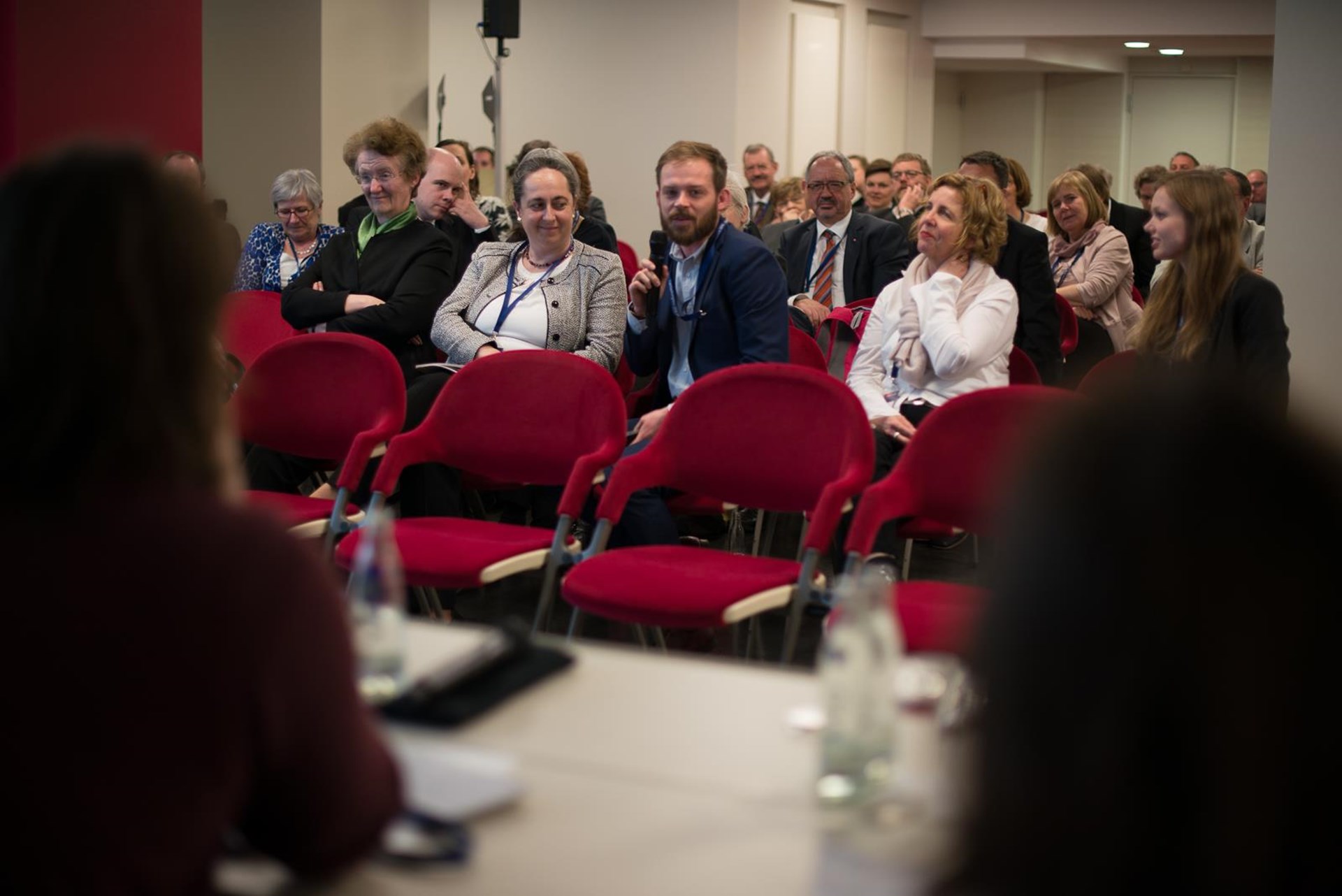 Zuschauer in einem Konferenzraum, einige Personen hören aufmerksam zu, während andere sich unterhalten.