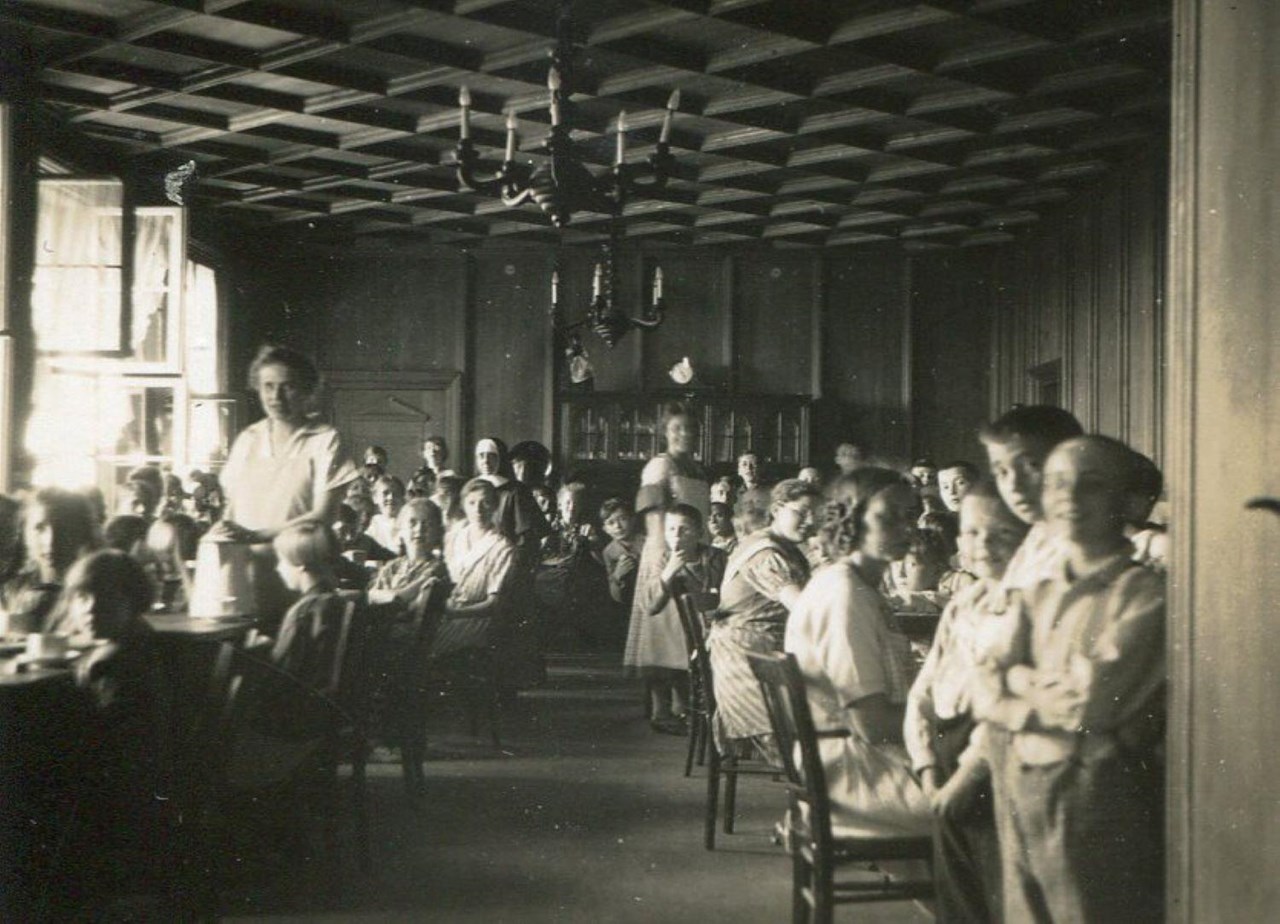 Viele Kinder sitzen an Tischen und werden mit Essen und Trinken versorgt.
