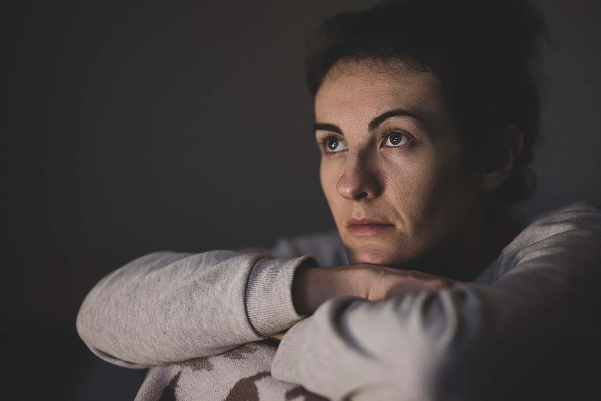 Eine junge Frau stützt ihren Kopf auf ihre verschränkten Arme und schaut fragend.