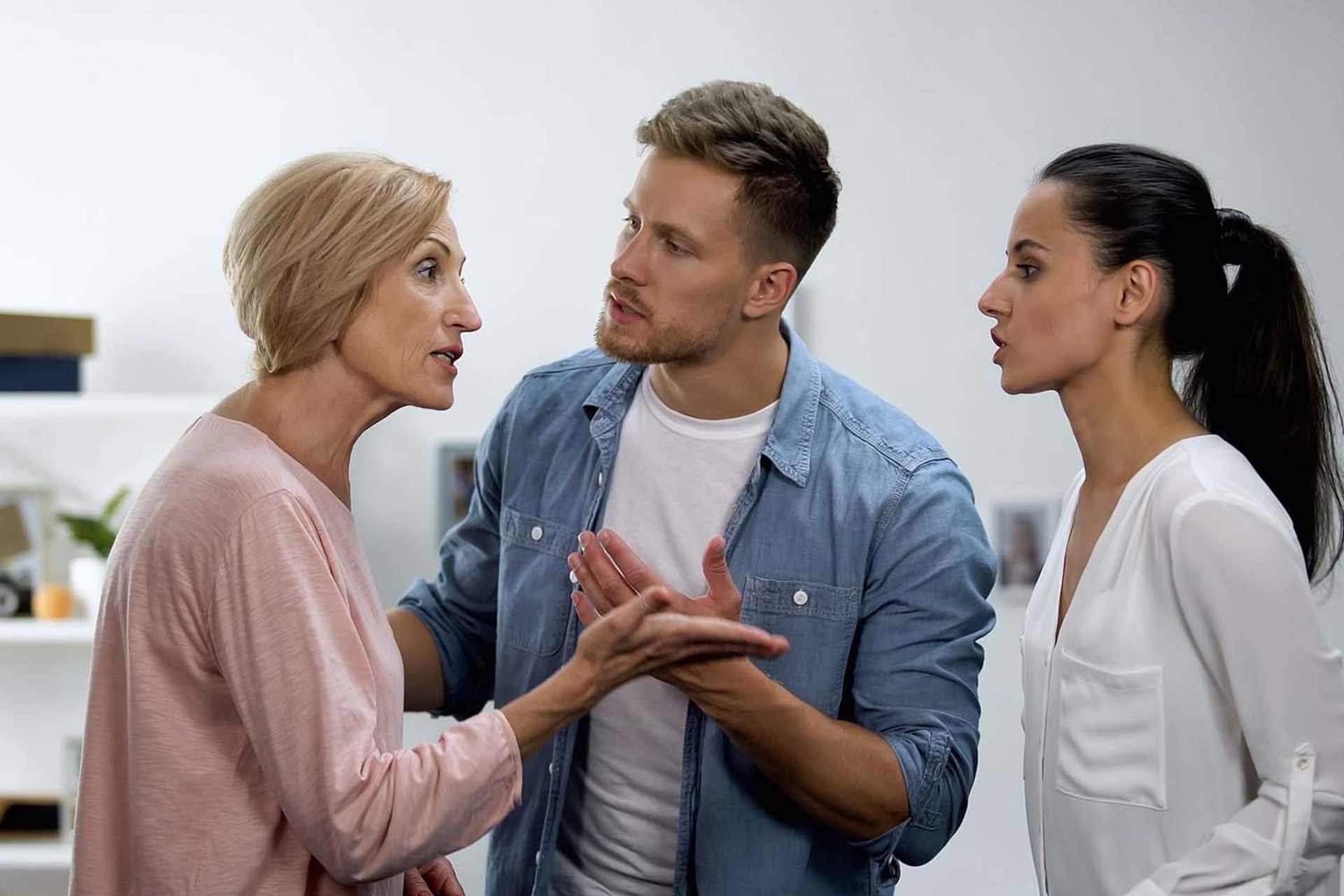 Drei Personen in einer angeregten Diskussion; eine ältere Frau spricht gestikulierend, ein Mann hört aufmerksam zu, während eine jüngere Frau ebenfalls mitteilt.