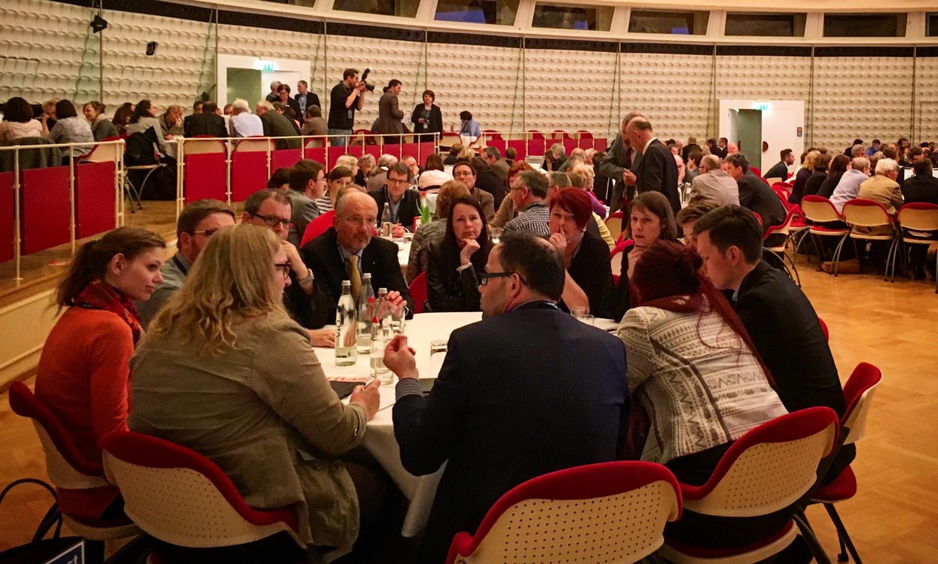 Eine Gruppe von Menschen sitzt an einem runden Tisch in einem Konferenzraum und diskutiert. 
