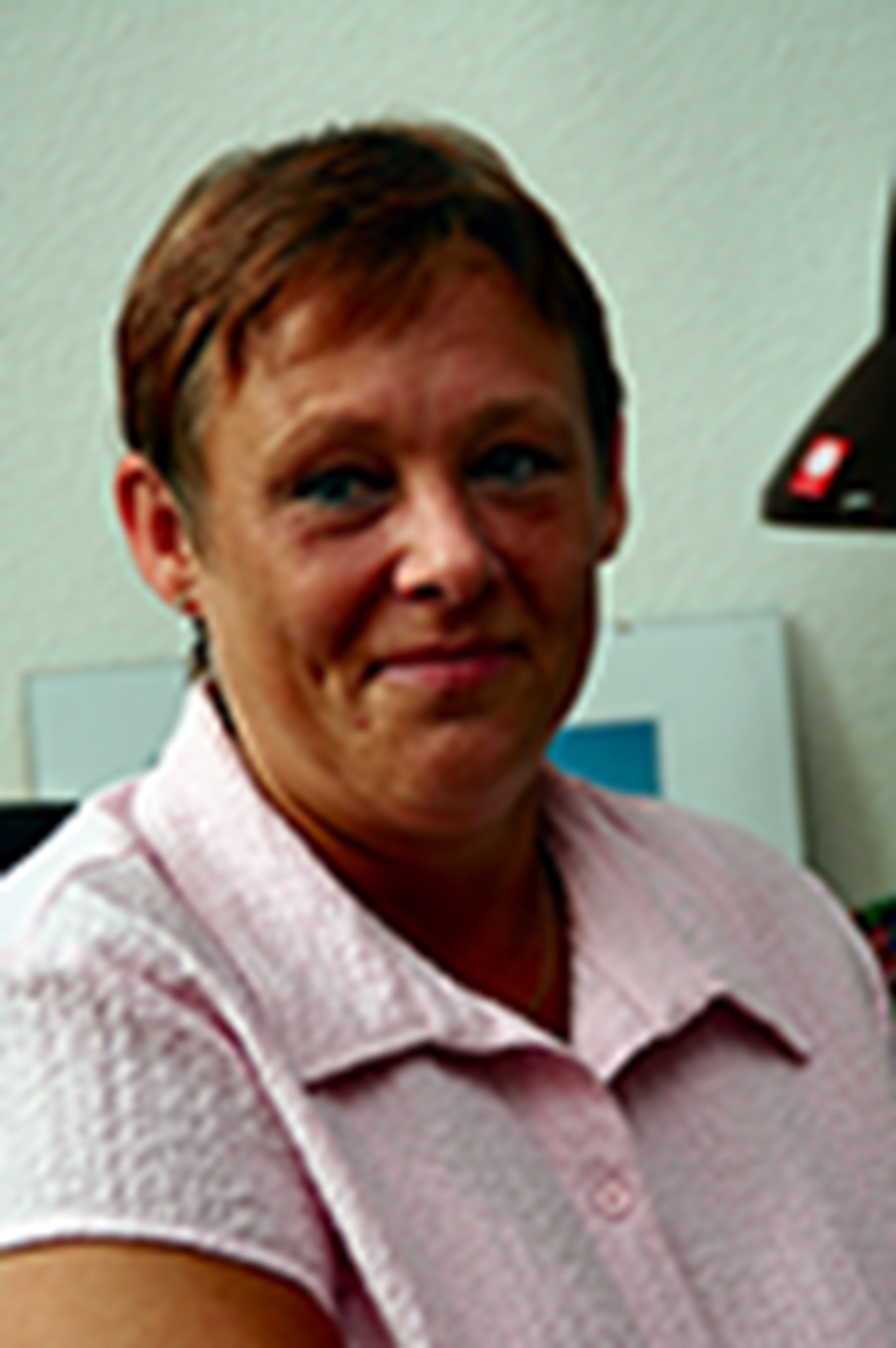 Lächelnde Frau mit braunen Haaren, die ein rosa Hemd trägt und in einem Büro sitzt