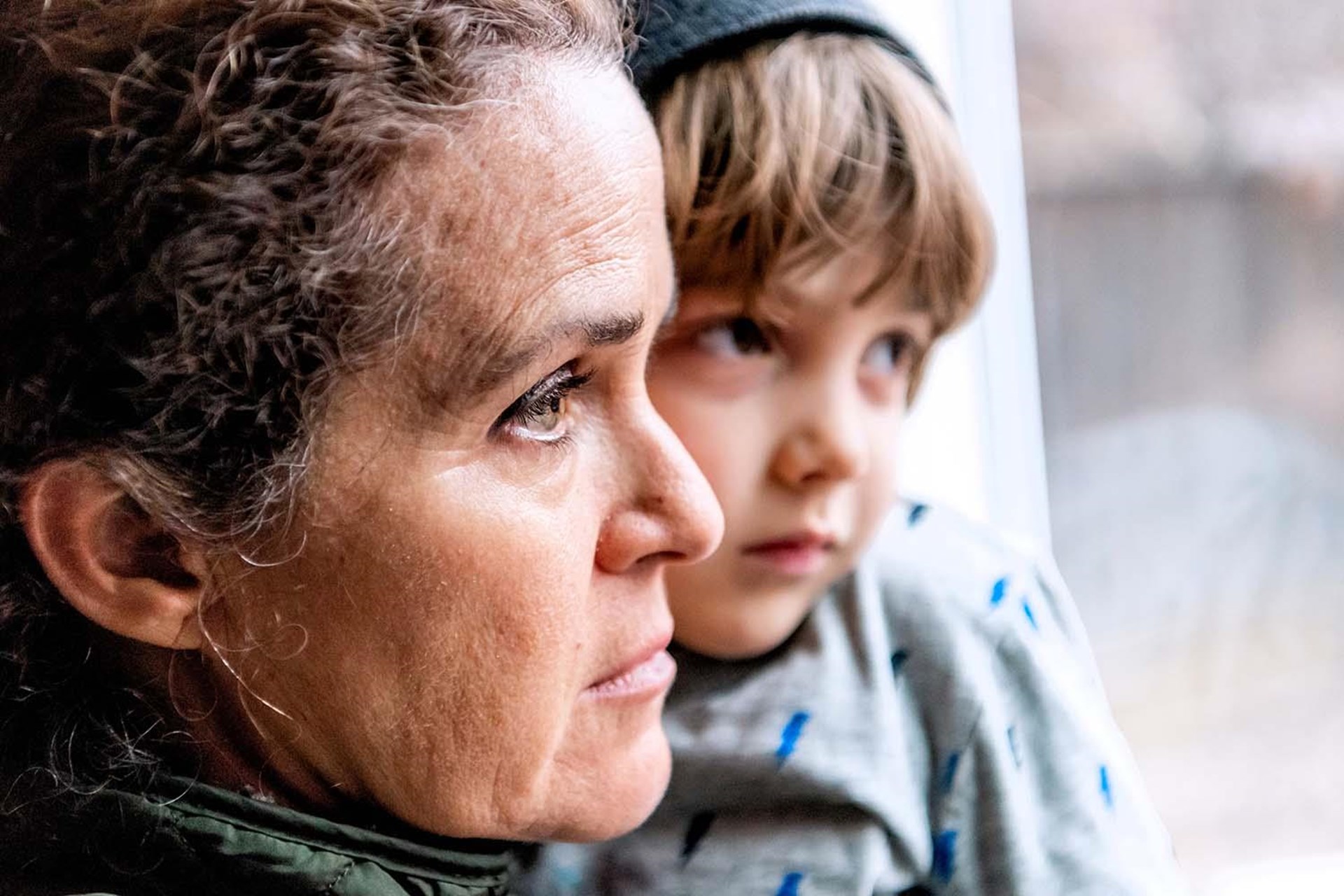 Eine Frau blickt entmutigt aus einem Fenster und hat einen kleinen Jungen auf dem Arm