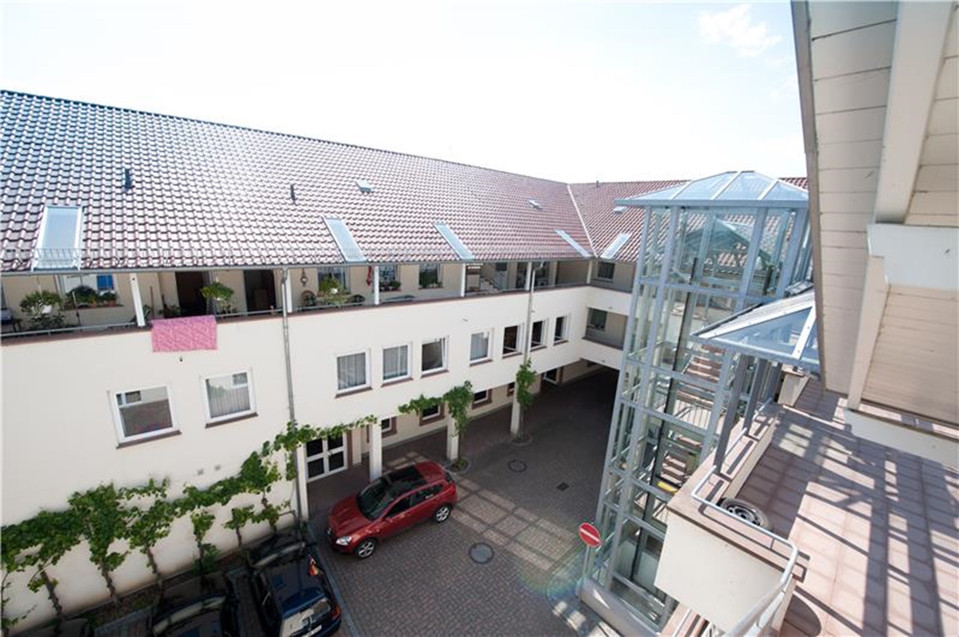 Innenhof eines Wohngebäudes mit roten und schwarzen Autos, begrünten Wänden und einem gläsernen Aufzug.