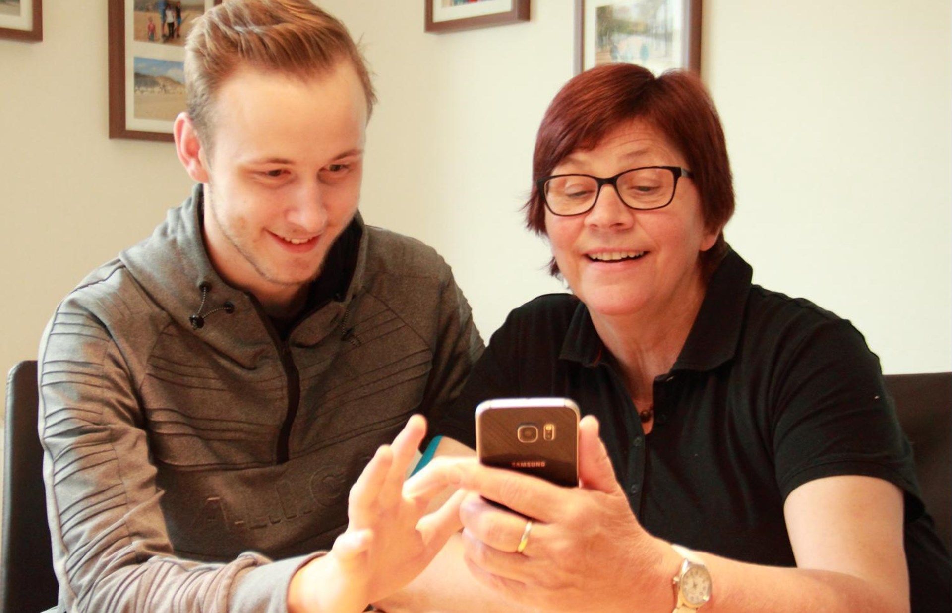 Ein junger Mann unterrichtet eine ältere Dame in der Smartphone-Nutzung.
