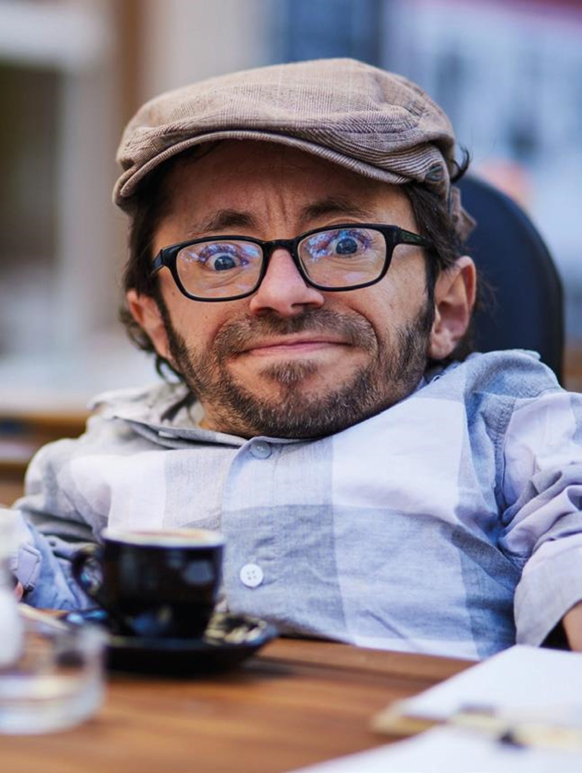Das zeigt den Inklusionsaktivisten Raúl Krauthausen. einen kleinen Mann mit Brille und Schidbermütze. Vor ihm steht eine Espressotasse. 