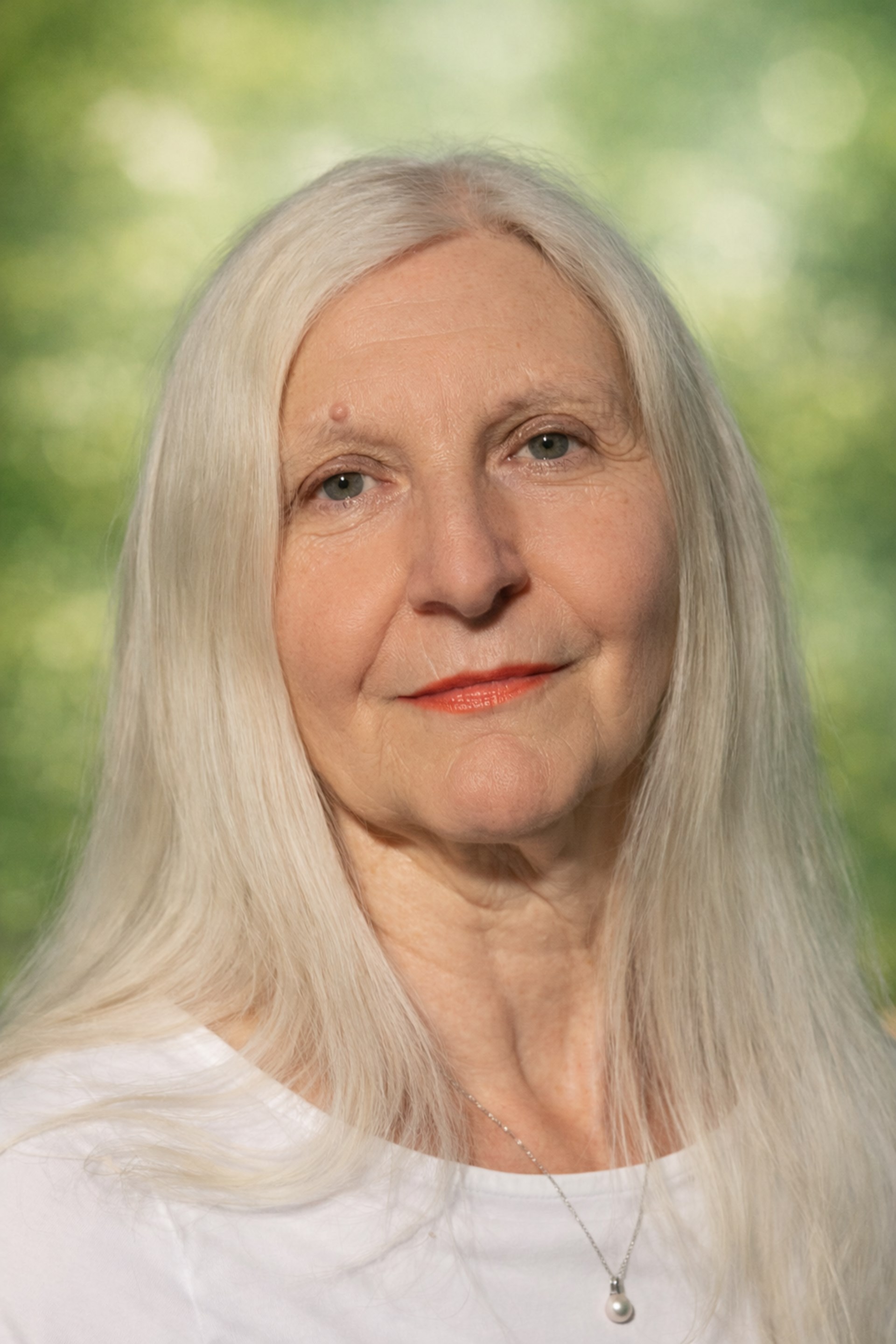 Porträtfoto einer Frau mit langen weiß-grauen Haaren in weißem Shirt; im Hintergrund unscharf grüne Bäume und die Silhouette des Wormser Doms