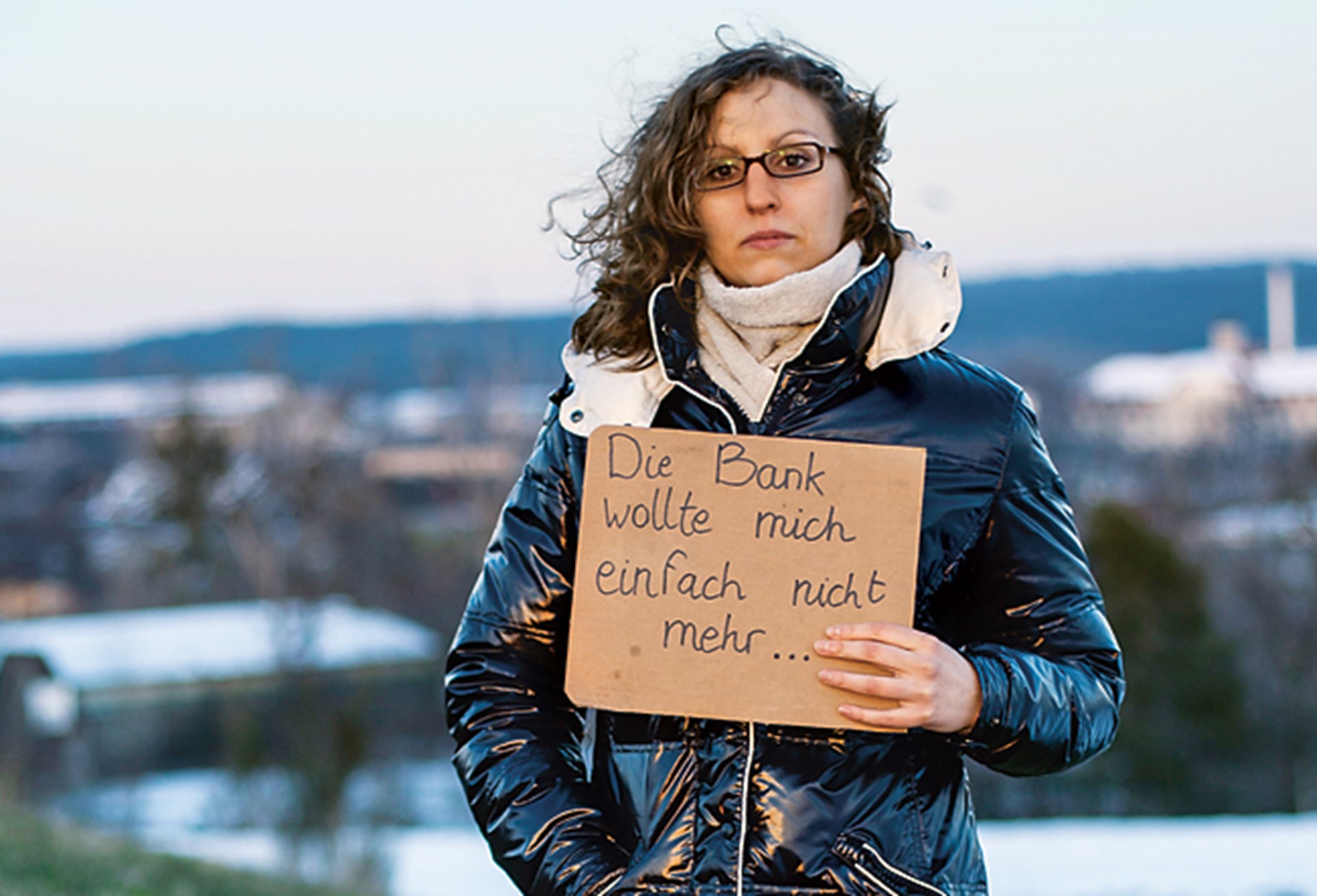 Junge Frau hält einen Karton mit der Aufschrift "Die Bank wollte mich einfach nicht mehr"
