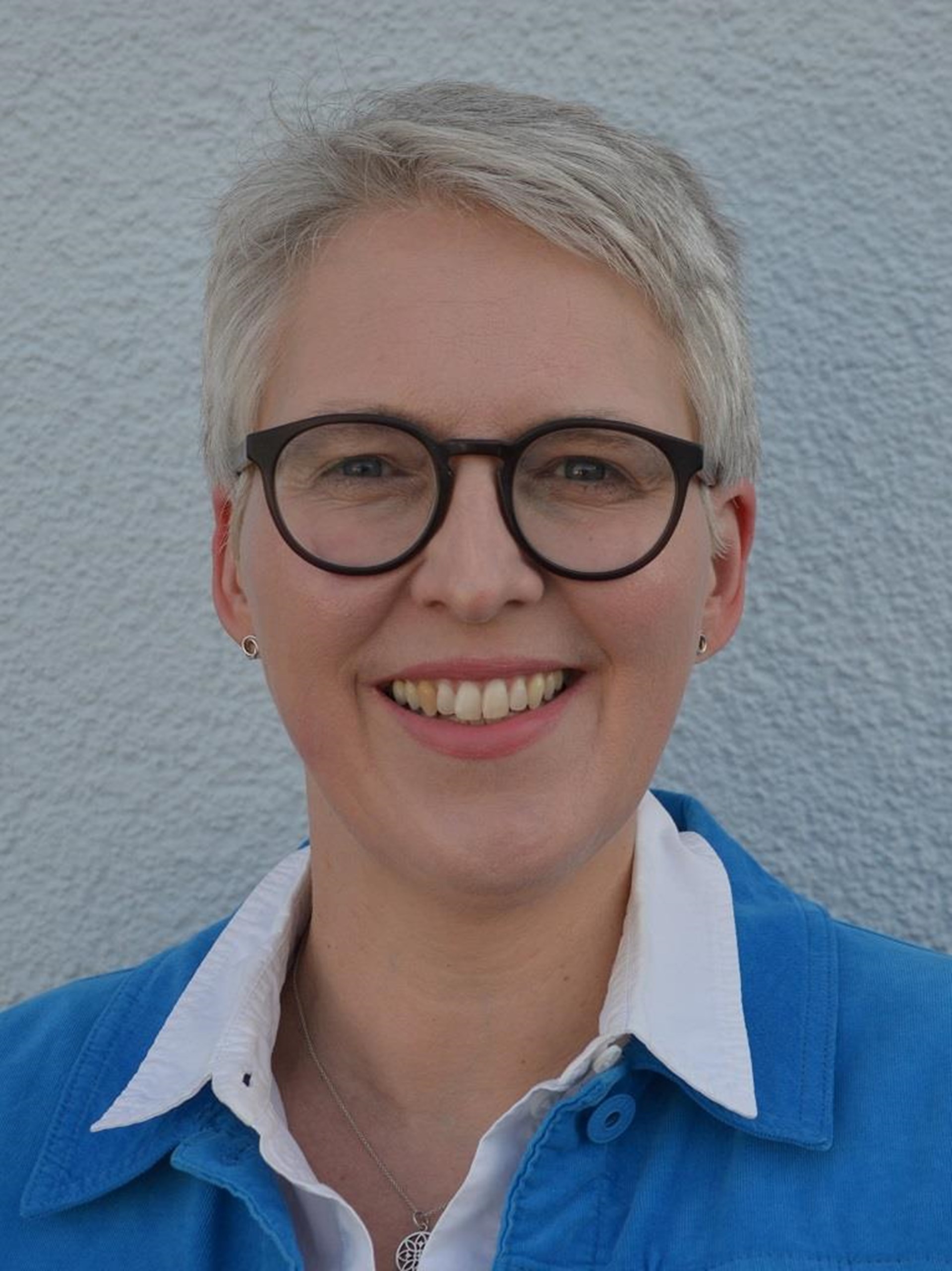 Frau mit kurzen grauen Haaren und Brille im Porträt.