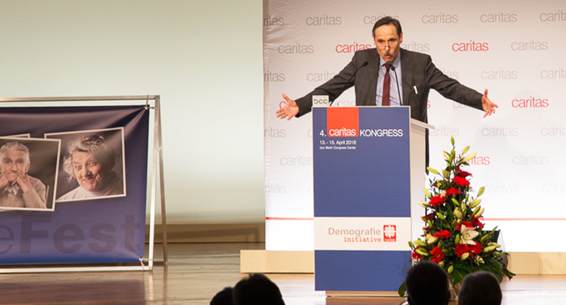 Mann spricht am Rednerpult auf dem Caritas Kongress, im Hintergrund Bilder von älteren Menschen und eine Blumendekoration.