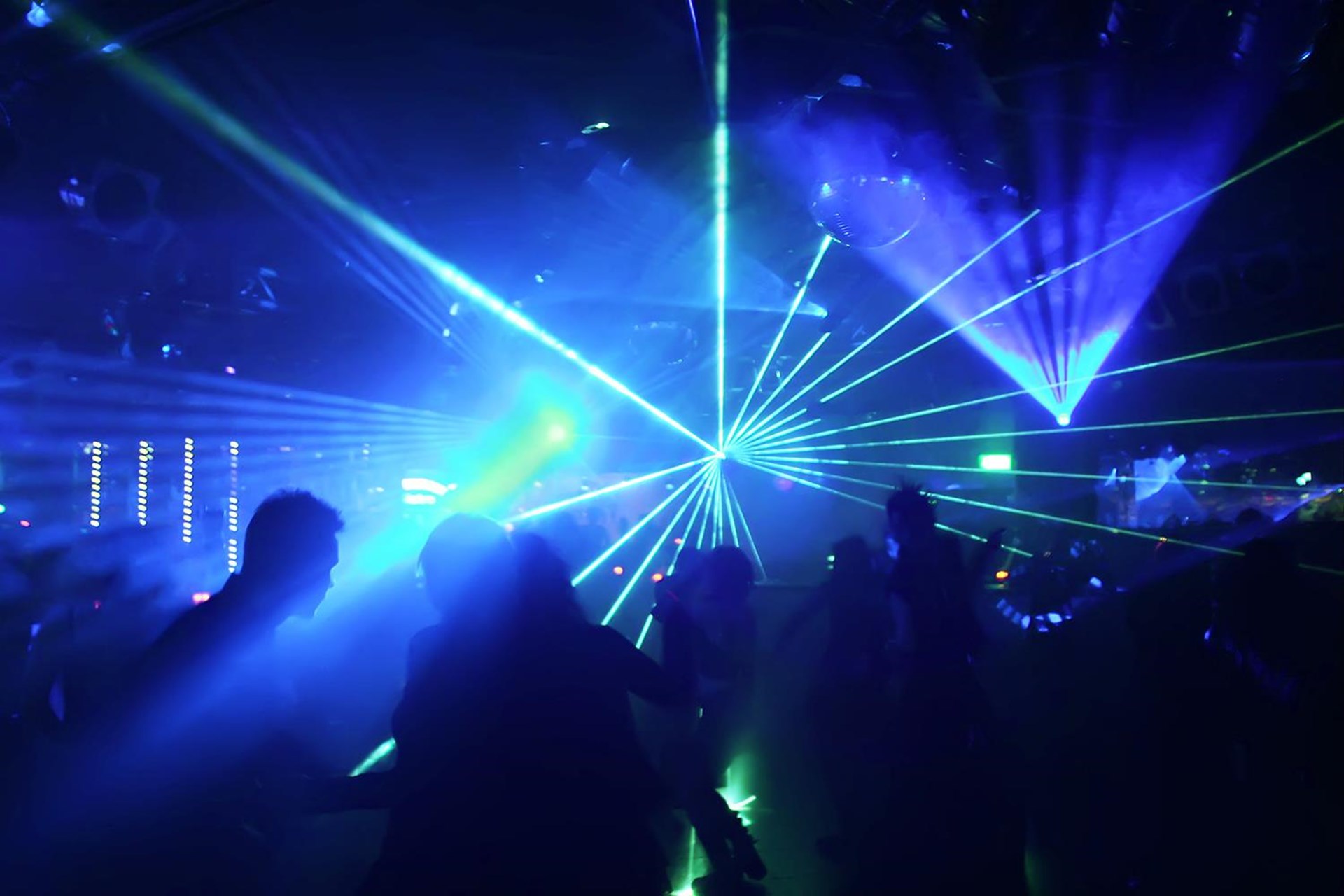 Nachtclub-Szene mit bunten Laserstrahlen und tanzenden Menschen im Vordergrund. Die Lichtshow erzeugt eine dynamische und energetische Atmosphäre.
