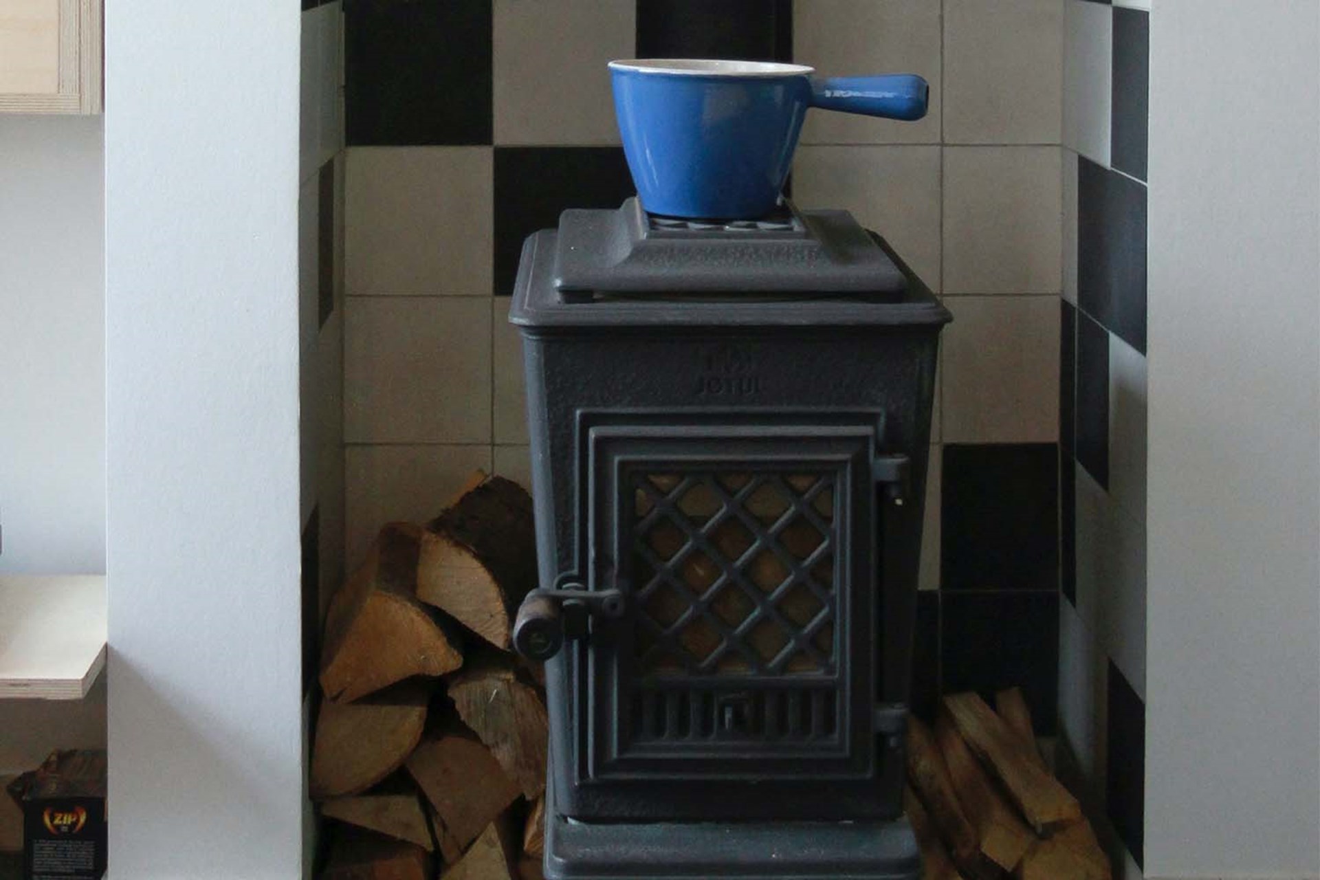 Ein Holzofen in einer Wohnung vor einer gekachelten Nische mit einem blauen Topf darauf.
