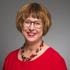 Lächelnde Frau mit braunen Haaren und Brille, die ein rotes T-Shirt und eine Halskette mit bunten Steinen trägt