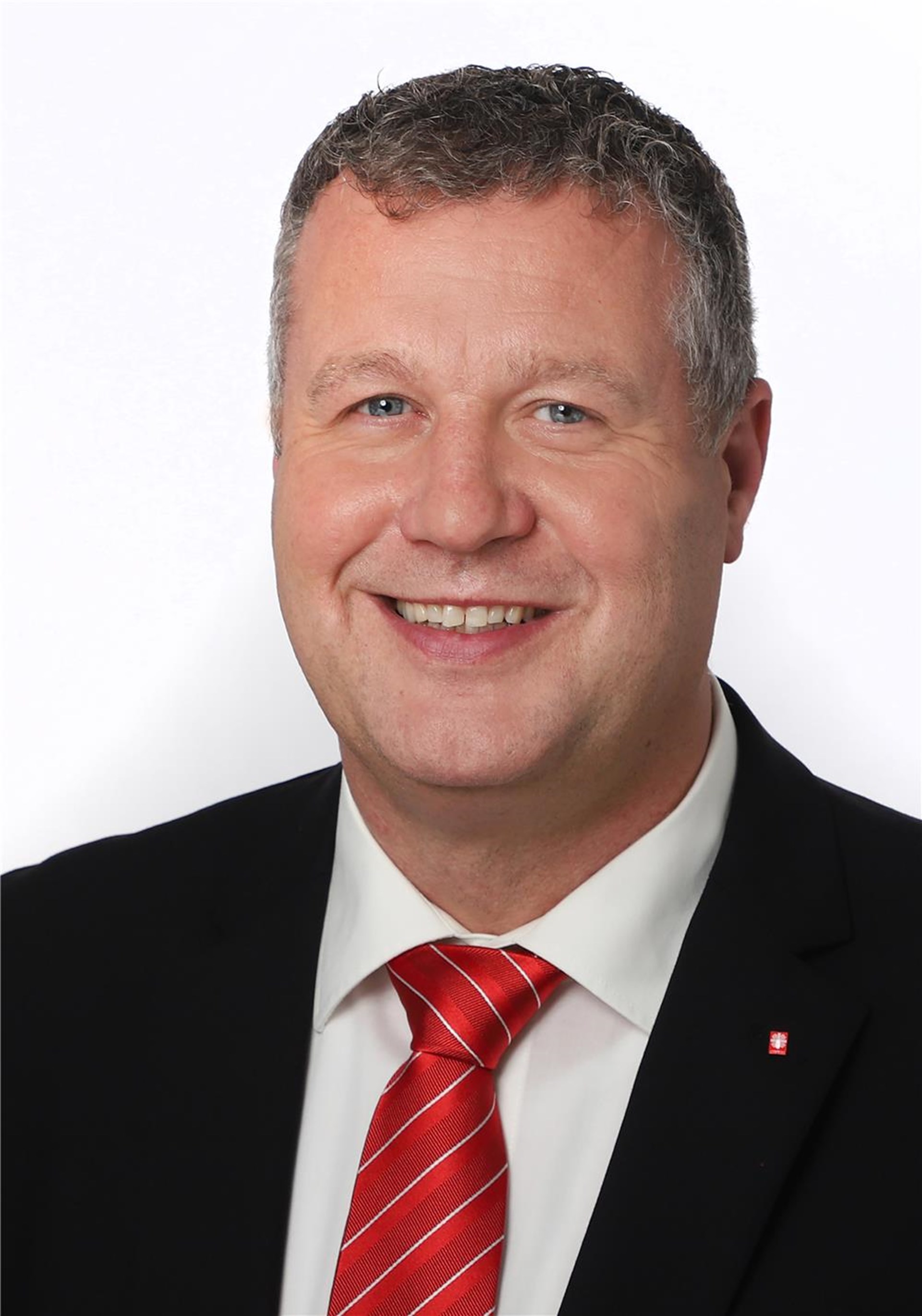 Ein Mann mit Anzug und roter Krawatte lächelt in die Kamera.