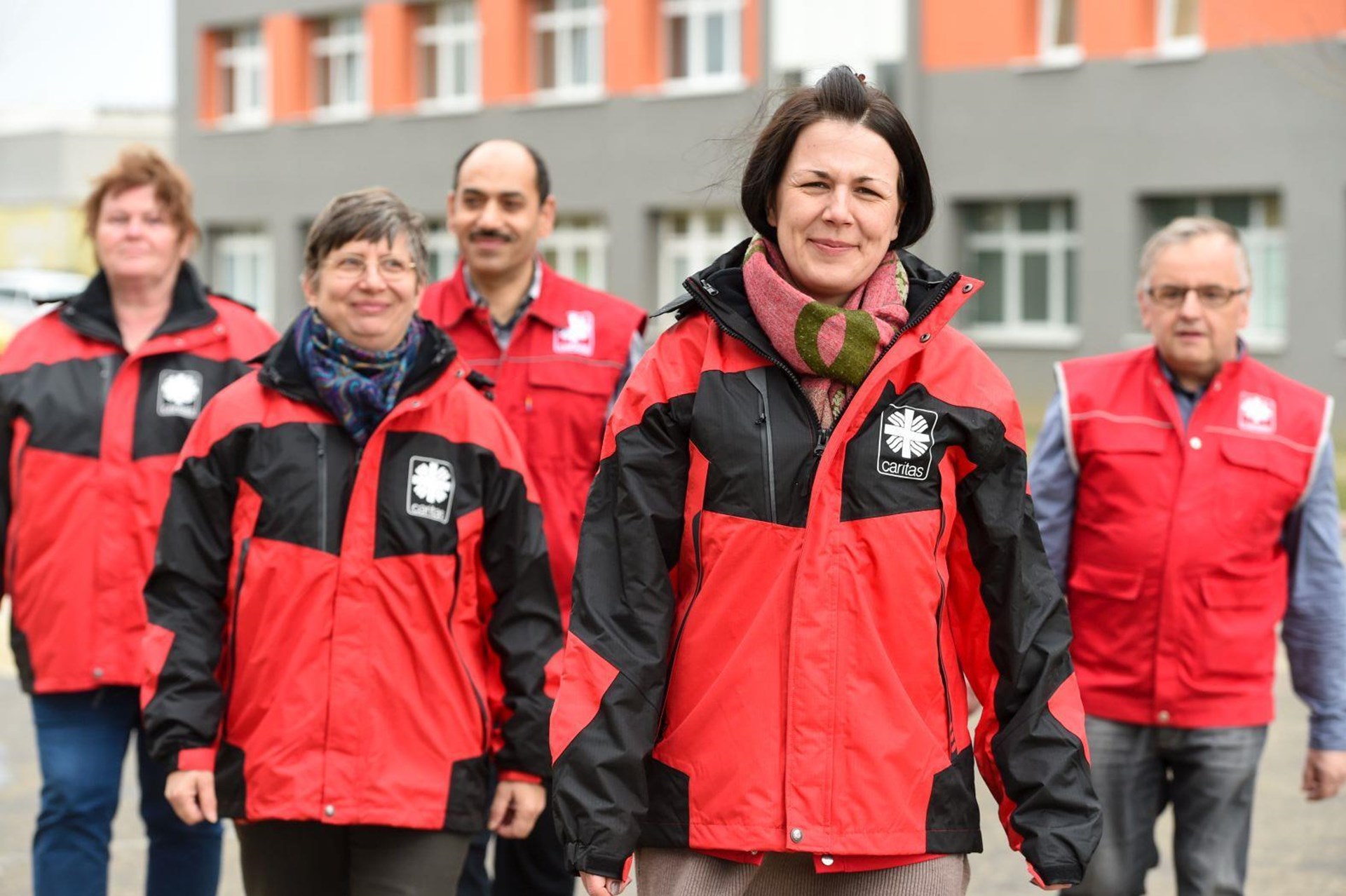 Gruppe von fünf Personen in roten und schwarzen Jacken, die gemeinsam draußen gehen. 