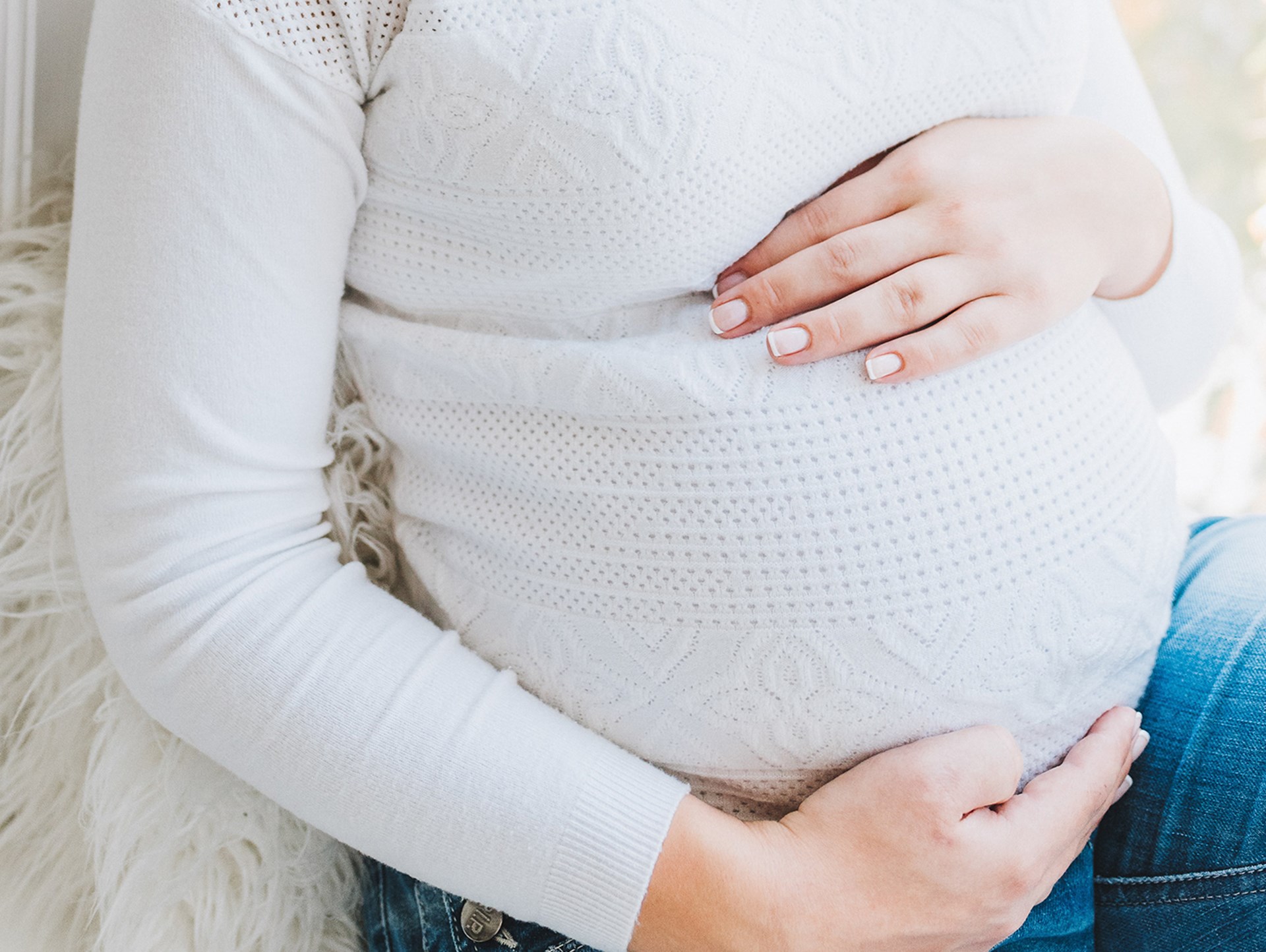 Ein Schwangerschaftsbauch einer Frau mit weißen Pullover