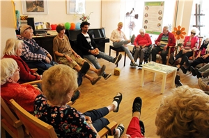 Eine Gruppe mit älteren Menschen sitzt im Kreis und macht Bewegungsübungen.