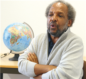 Porträt von Mussié Mesghinna. Neben ihm steht ein Globus auf einem Tisch.