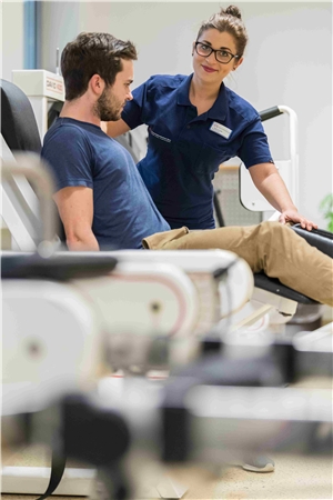 Eine Physiotherapeutin weist einen Patienten in die Nutzung eines Fitness-Geräts ein.