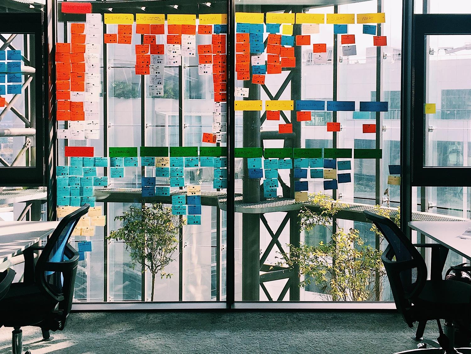 Fensterscheibe in einem Büro, an dem viele verschiedenfarbige Klebezettel hängen.