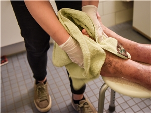Eine jüngere jüngere Person wäscht die Füße einer pflegebedürftigen älteren.