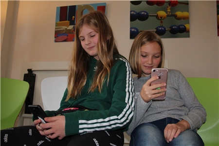 Zwei junge Mädchen, die in ein Smartphone schauen.