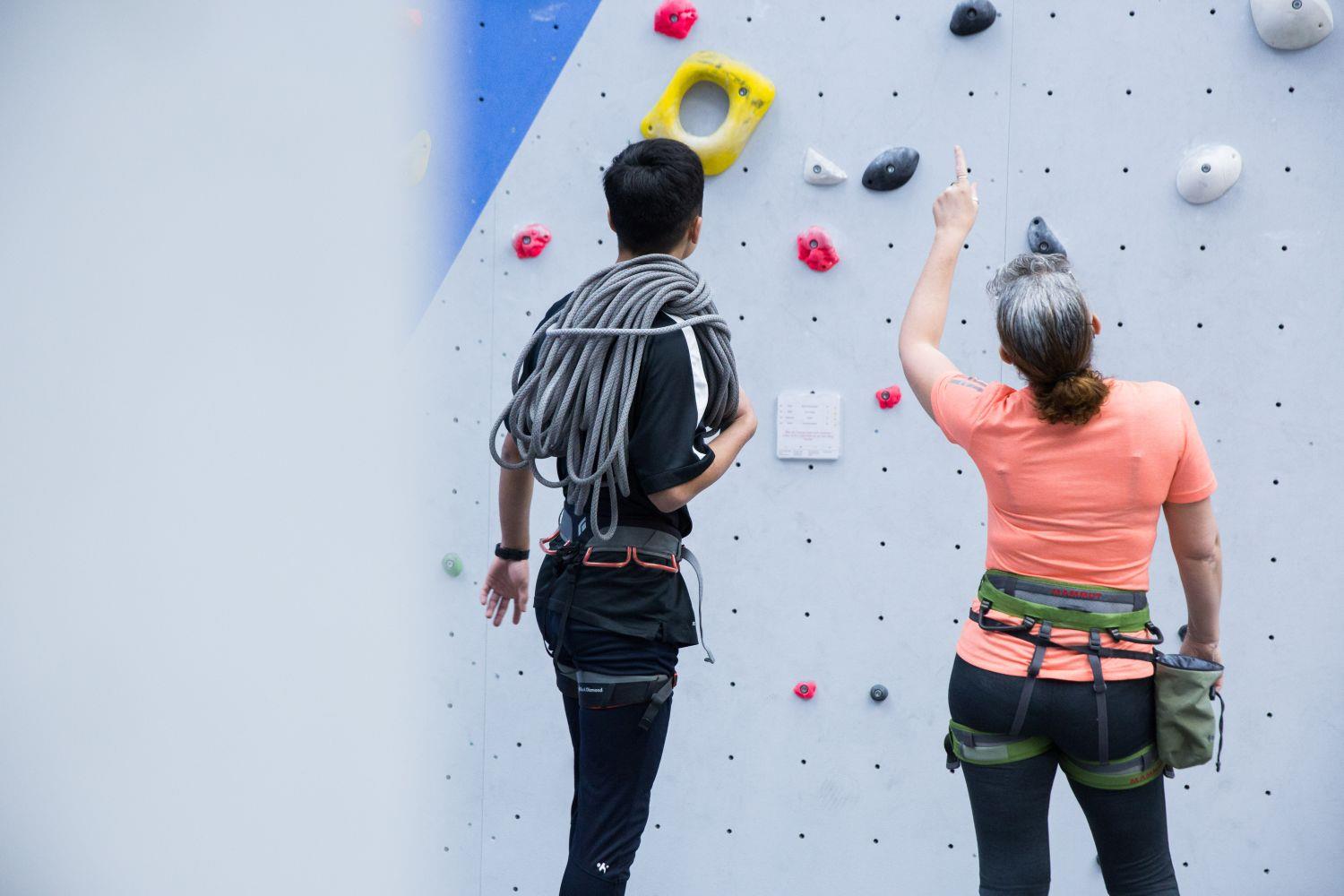 Junger Mann und Frau stehen vor einer großen Kletterwand