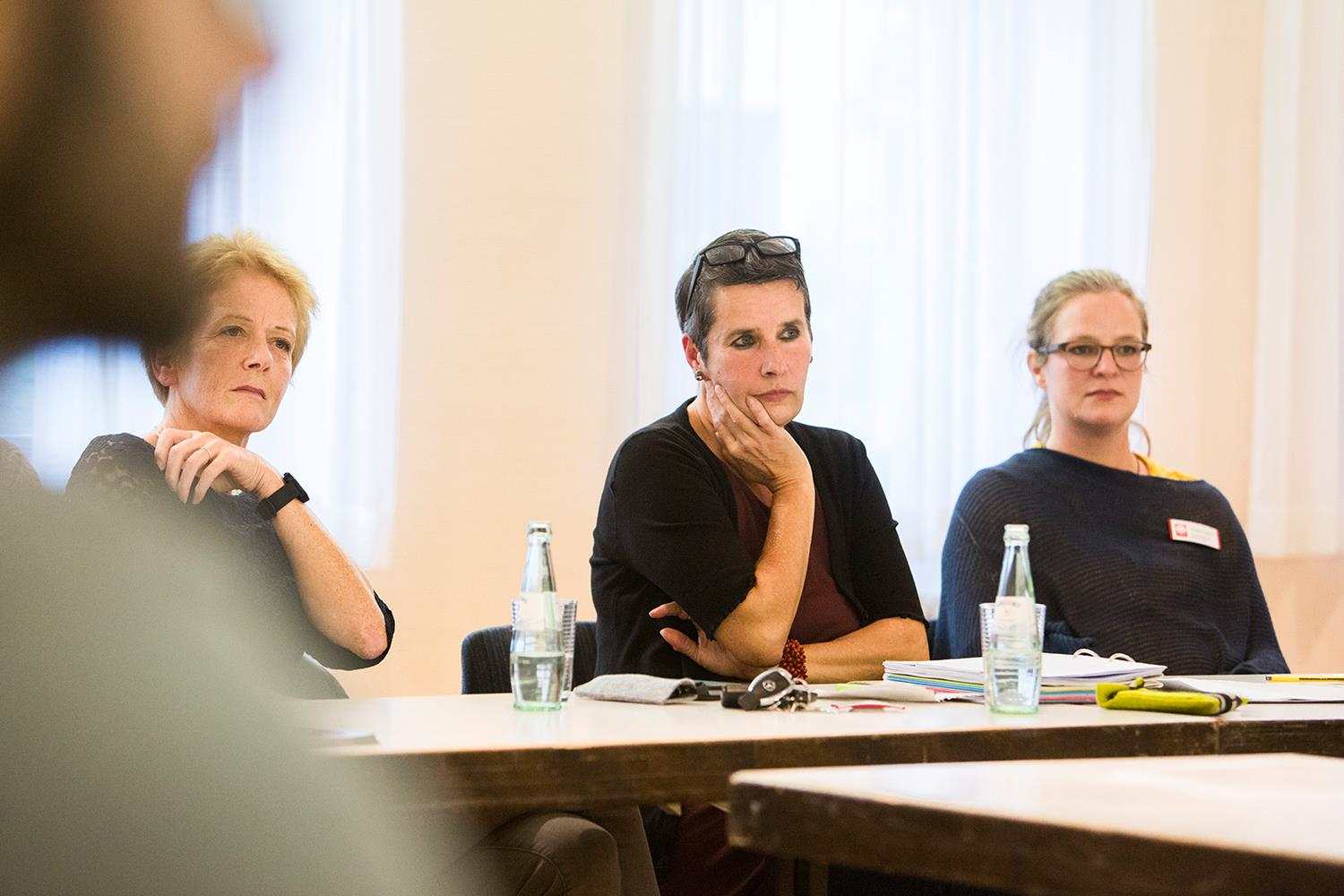 Drei Frauen sitzen an einem Tisch und hören etwas oder jemandem außerhalb des Bildes zu