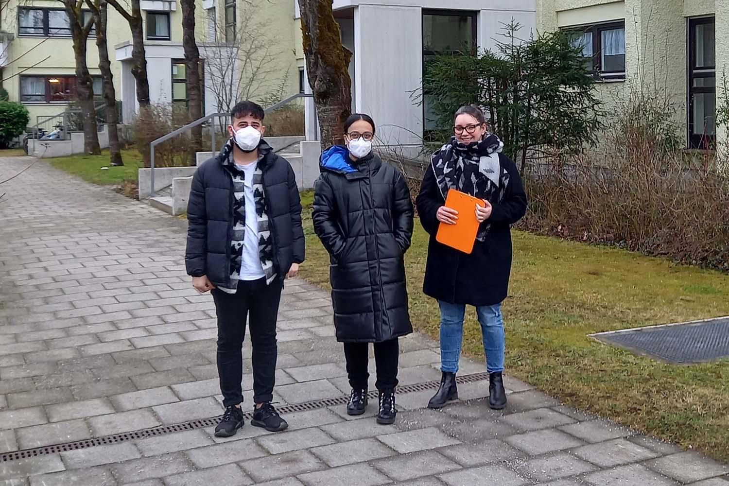 Drei Personen stehen vor einem Wohngebäude