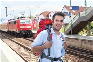 Lächelnder Mann mit Wanderrucksack am Bahnsteig