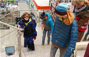 Jugendliche mit Alterssimulations-Anzug und Seheinschränkungsbrille ersteigen mühsam eine Treppe im Supermarkt.