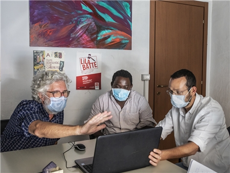 Drei Männer mit Mundschutz vor einem Laptop