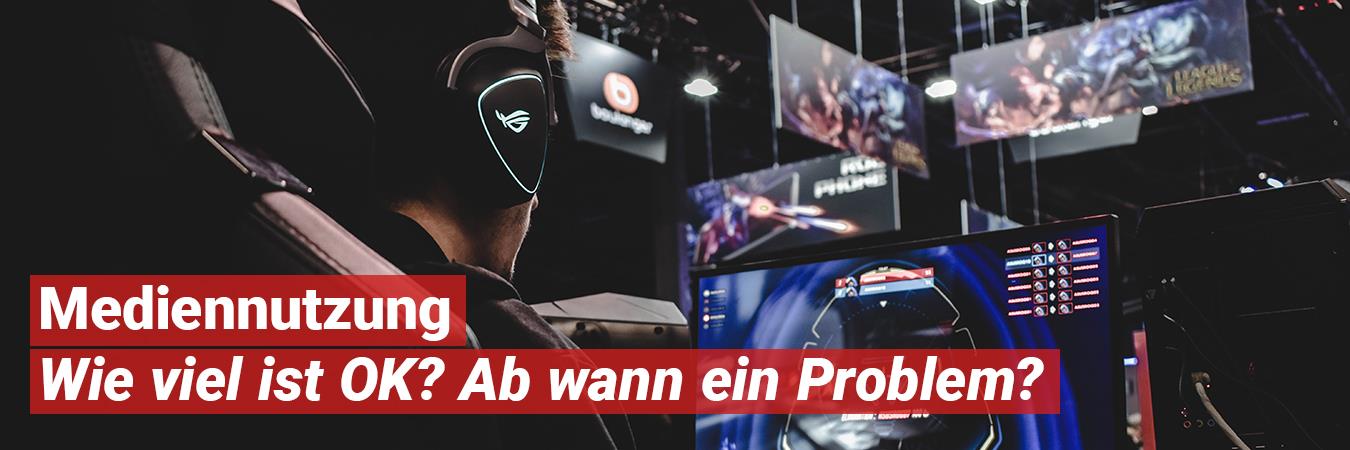Ein Junge sitzt vor mehreren Computerbildschirmen in einem abgedunkelten Raum.