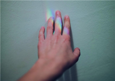 Eine Kinderhand vor einer Wand wird von den Regenbogenfarben eines Prismas beleuchtet.