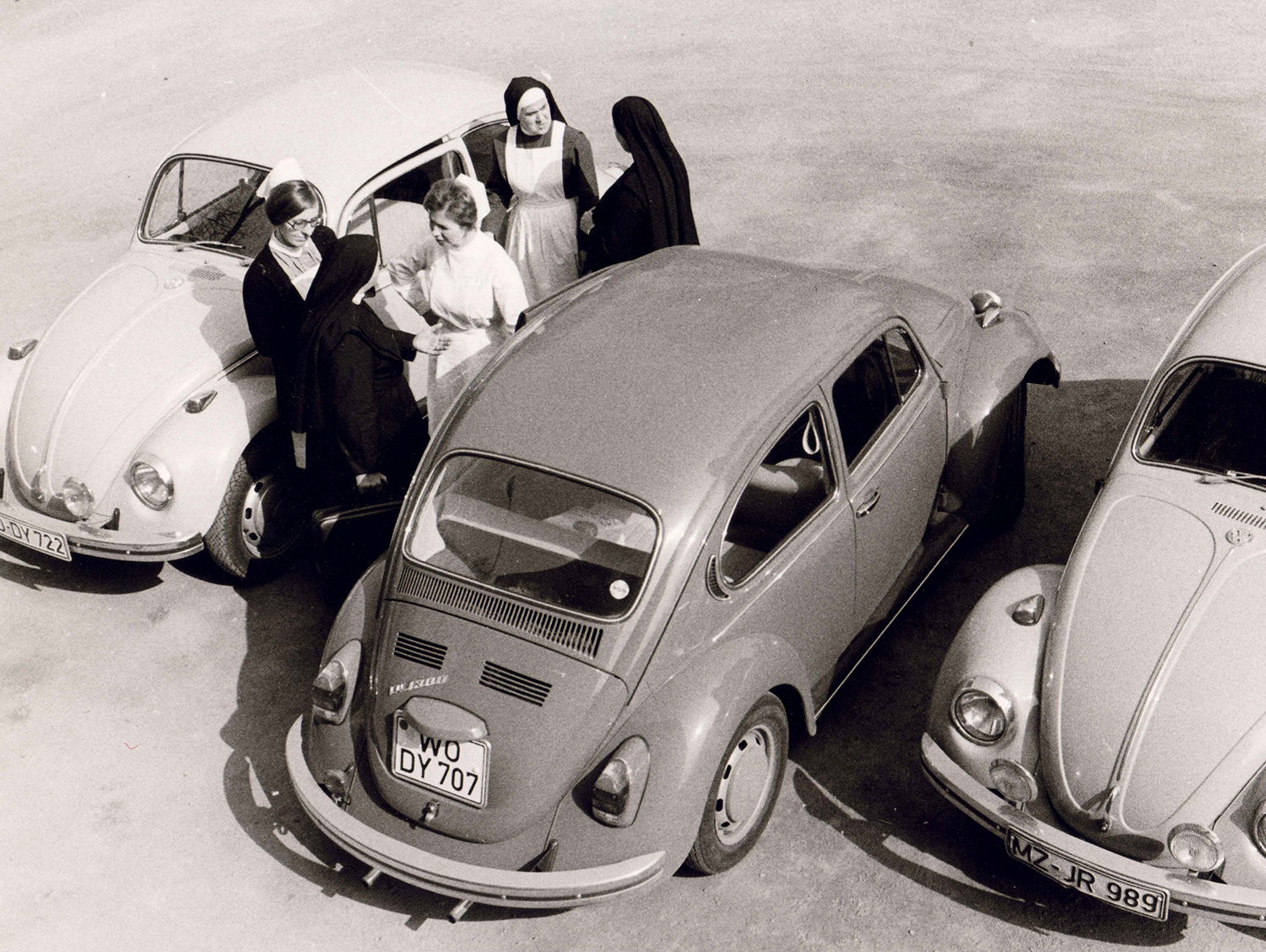 Drei alte Autos stehen auf der Straße, Fünf Ordensschwester stehen zwischen den Autos und reden.