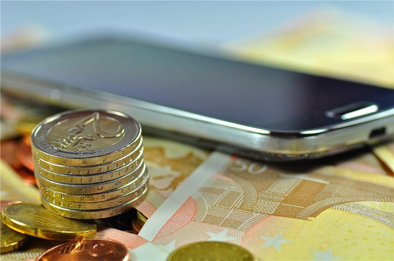 Smartphone liegt auf Geldscheinen und Münzen