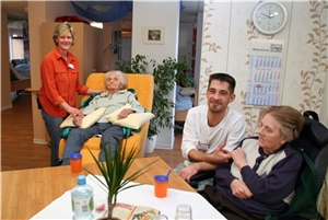 Auf dem Foto sitzen zwei Bewohner, die Pflegemitarbeiter kümmern sich um sie.
