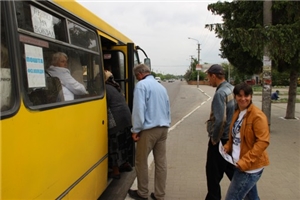 Ein gelber Bus hält an der Bushaltestelle. Er hat seine Tür zum Einsteigen geöffnet. 4 Menschen wollen noch mitfahren. 