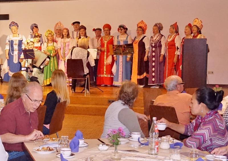 Gäste im Gemeindesaal lauschen dem russischen Chor. Die Chormitglieder tragen traditionelle russische Tracht in vielen Farben. (Reinhard Biermann)