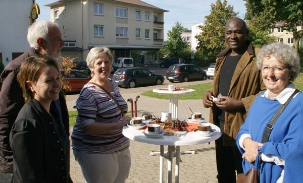 Gemeindemitglieder mit und ohne Migrationshintergrund unterhalten sich bei kleinen Snacks an einem Stehtisch im Freien. (Michael Junge)